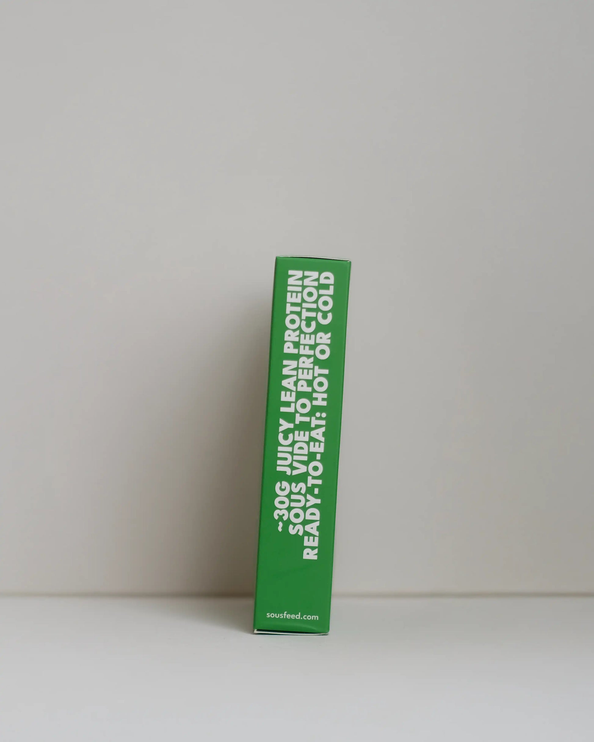 Side view of a SousFeed pesto alla genovese flavoured chicken breast and its light green packaging on a white background
