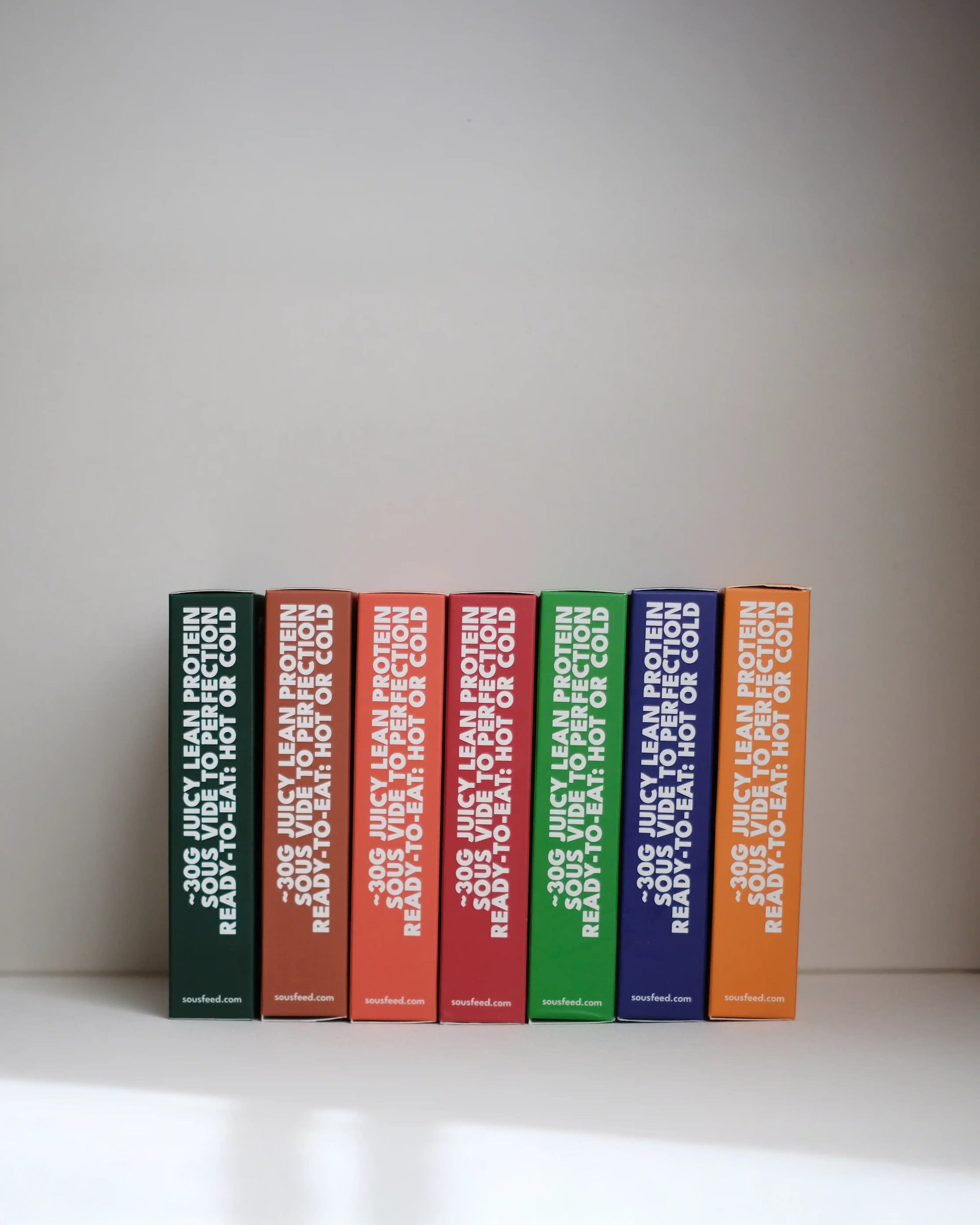 Side view of a set of SousFeed products in their boxes with colourful spines on a white surface and light gray background