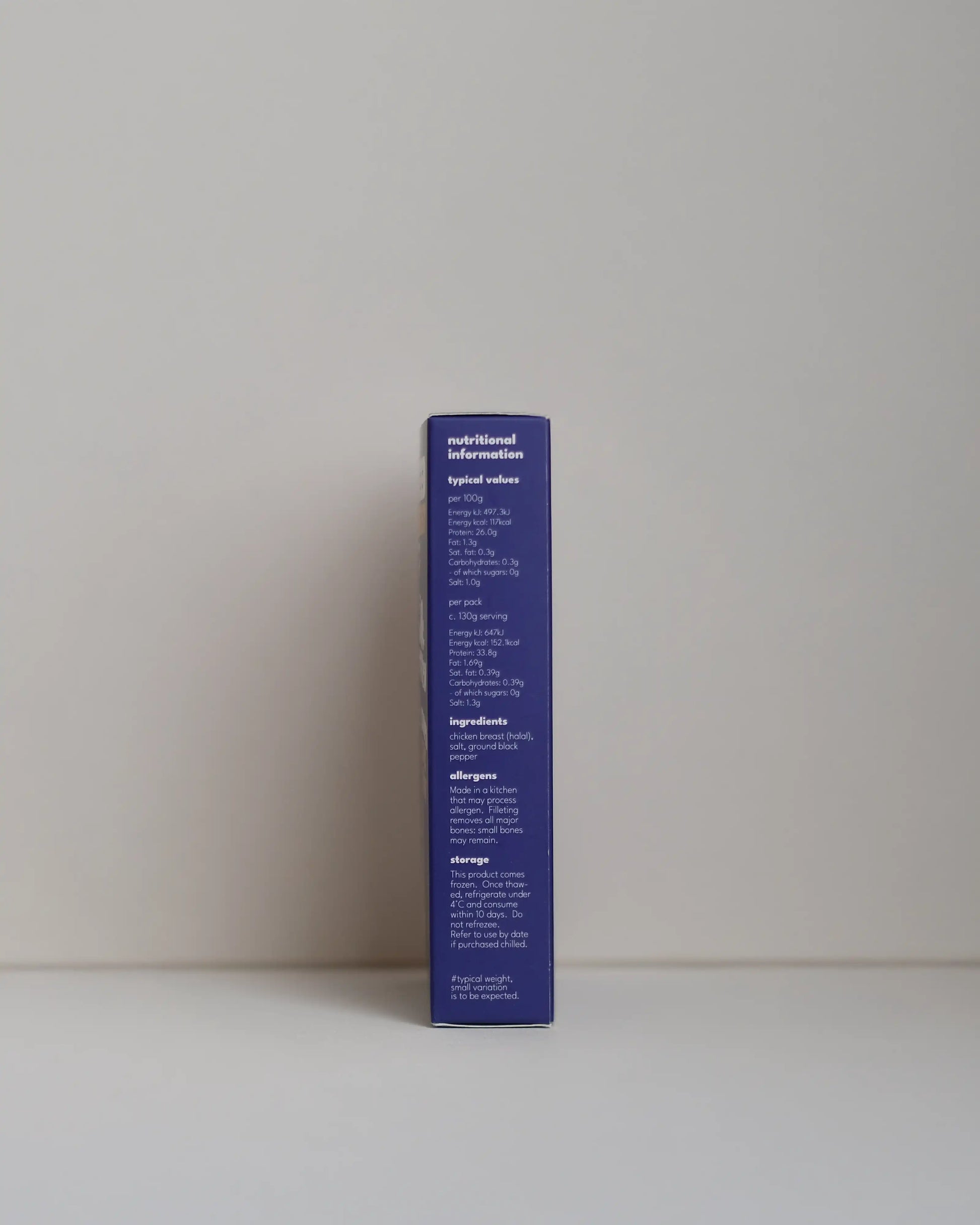 Side view of a SousFeed Salt and Pepper flavoured chicken breast and its purple packaging on a white background