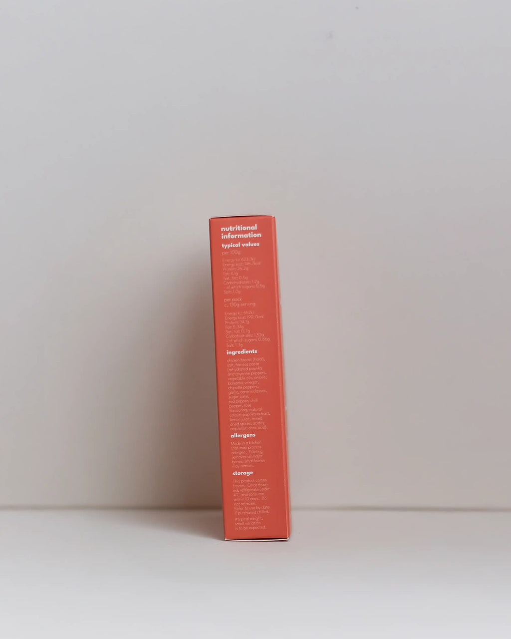 Side view of a SousFeed smoked harissa flavoured chicken breast and its red packaging on a white background