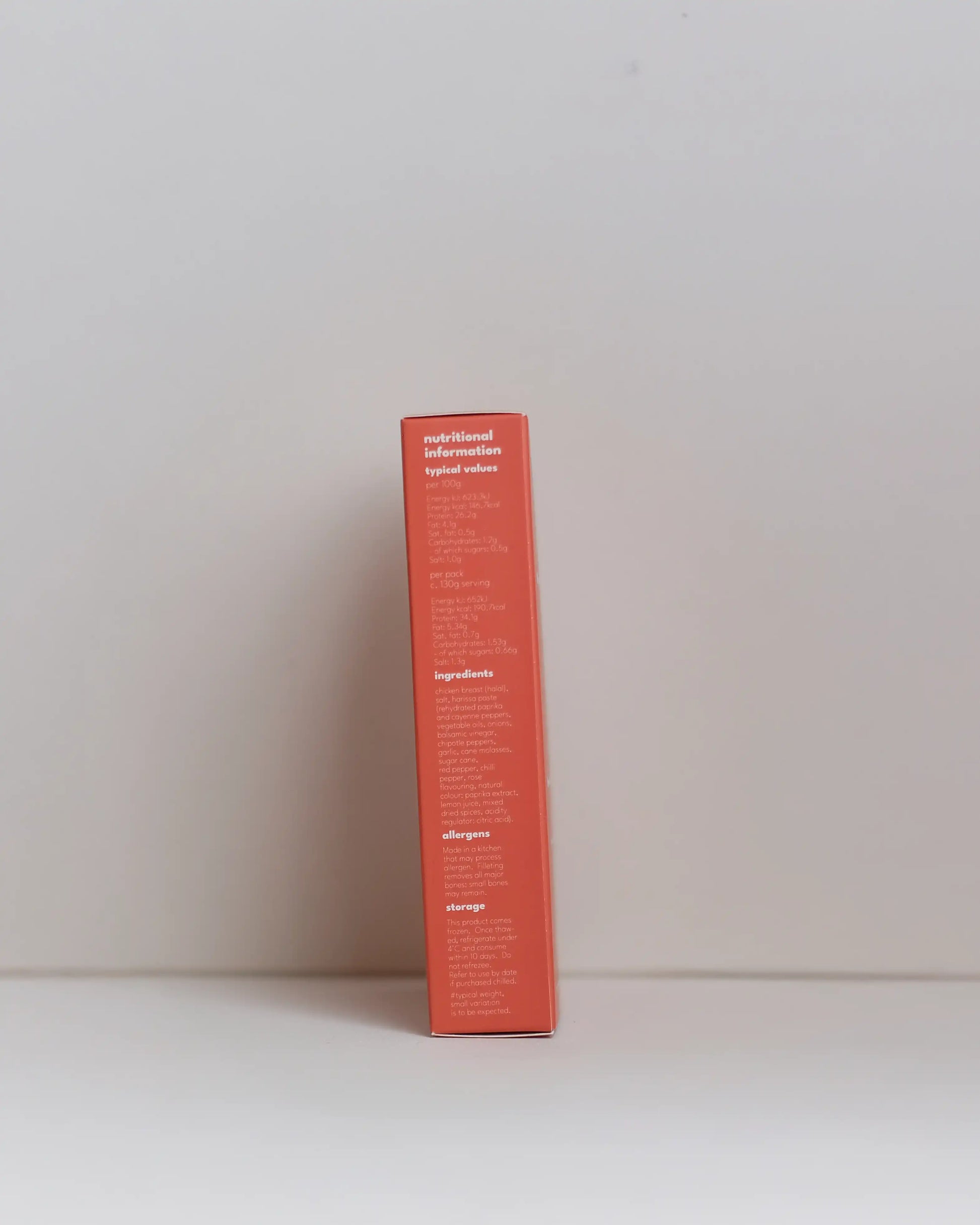 Side view of a SousFeed smoked harissa flavoured chicken breast and its red packaging on a white background