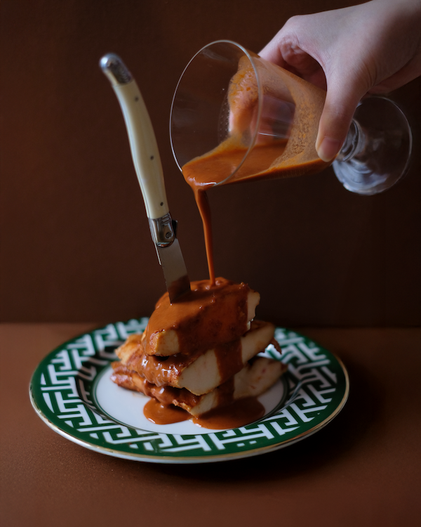 Pouring a sauce over sous vide chicken on a decorative plate with a knife.